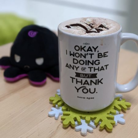 Mug full of hot chocolate with a quote from David Rose from the tv show "Schitt's Creek" on it next to a plush octopush toy